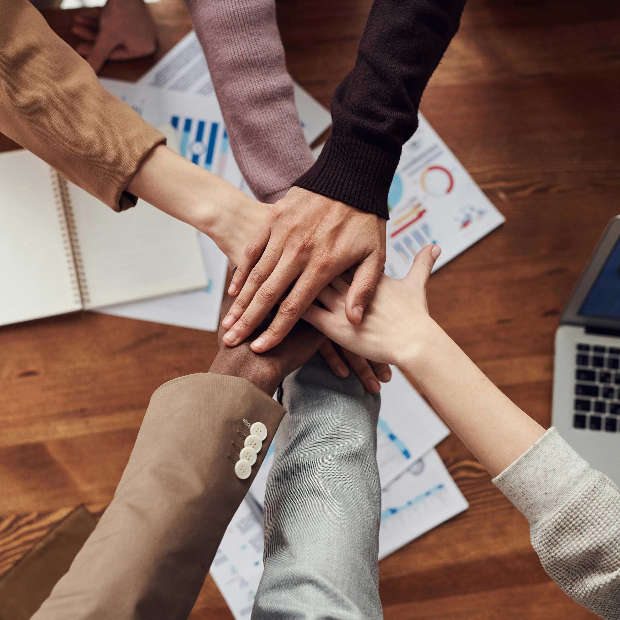 An image showing a group of people putting their hands together over financial documents to signify teamwork